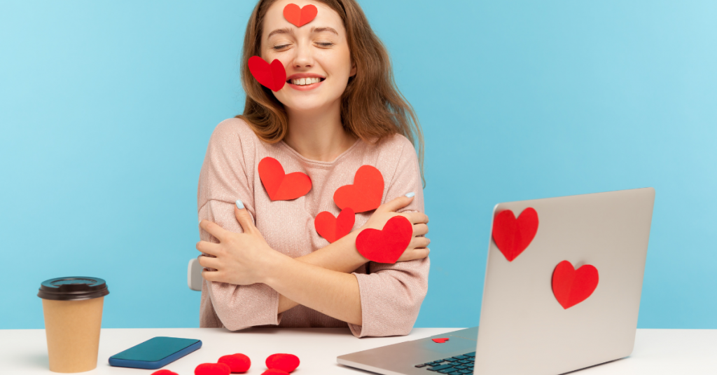 Woman at her laptop, hugging herself and covered in heart shaped stickers